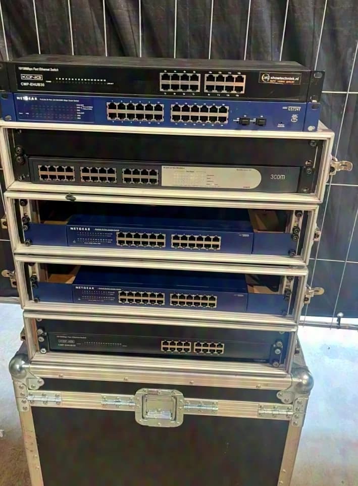 Diverse Netzwerk-Switches, darunter Modelle von Netgear und 3Com. Einige Geräte befinden sich in Flightcases.